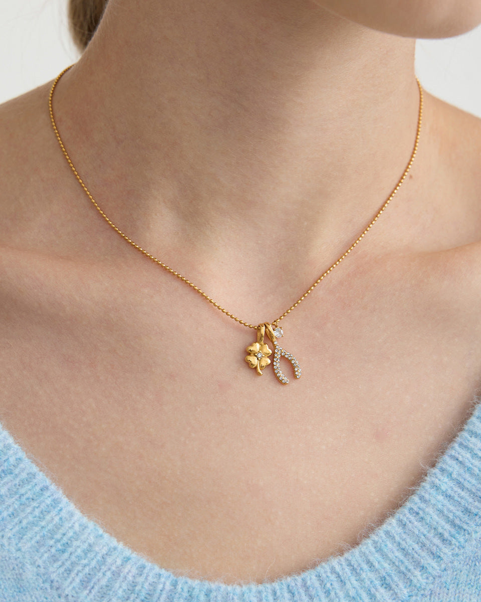 Gold necklace with a pendant on a person wearing a light blue sweater.