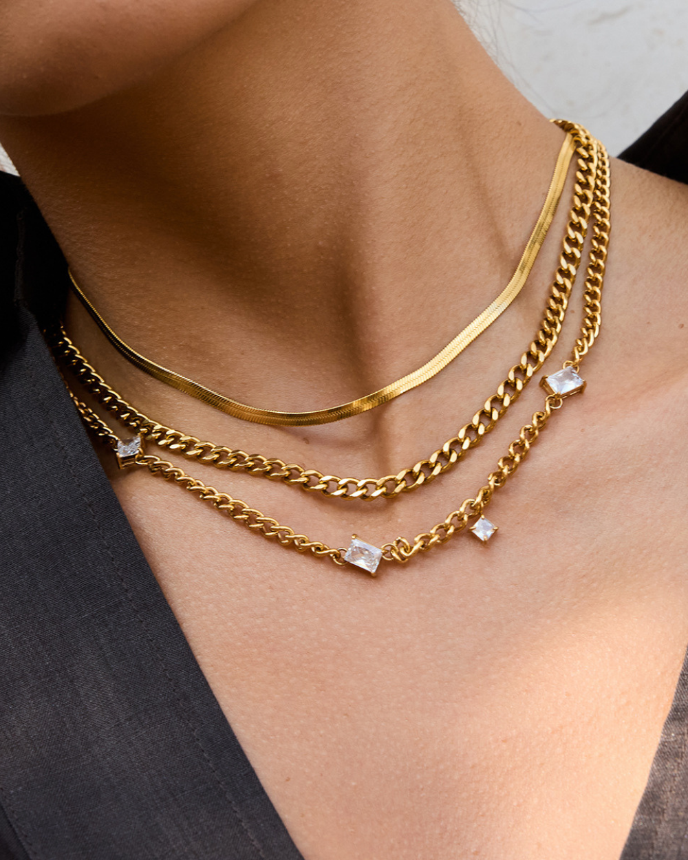 Gold chain necklaces with diamond pendants on a person wearing a black top.