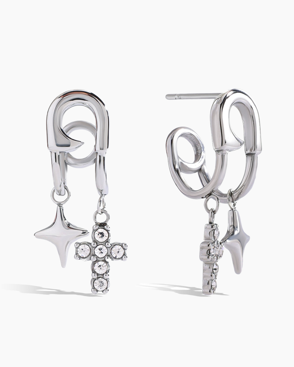 Pair of silver earrings with star, cross, and arrowhead charms on a white background