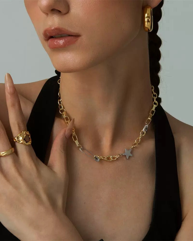 Woman wearing a gold necklace with star pendants, gold hoop earrings, and rings on a neutral background