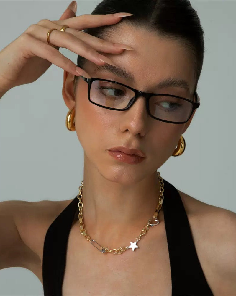Woman wearing glasses and gold jewelry against a neutral background