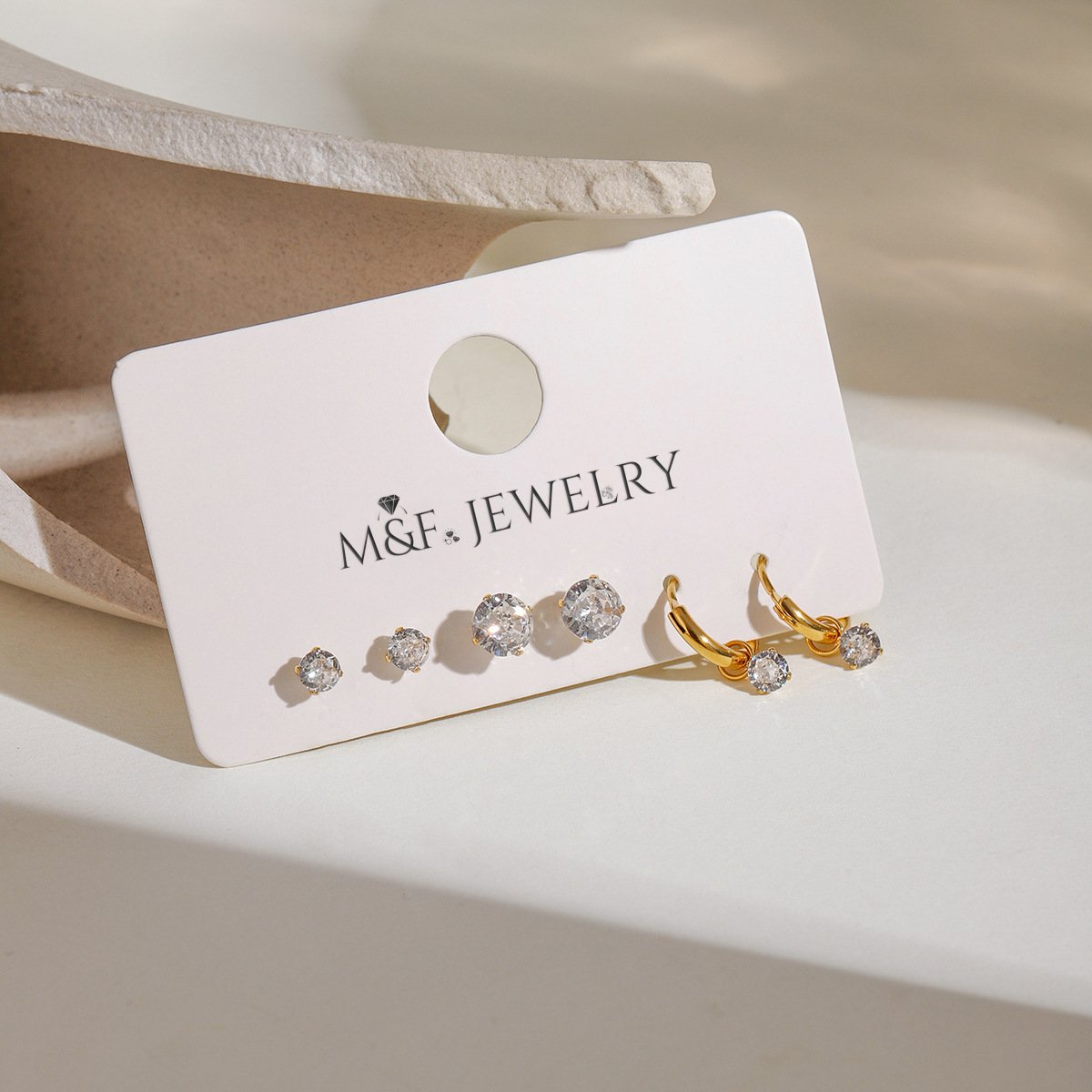 Gold hoop earrings and cubic zirconia studs displayed on a white card with M&F Jewelry logo
