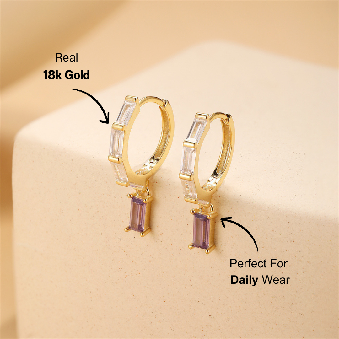 A close-up of 925 sterling silver drop earrings with gold plating and sparkling zirconia stones, displayed on a soft neutral background.