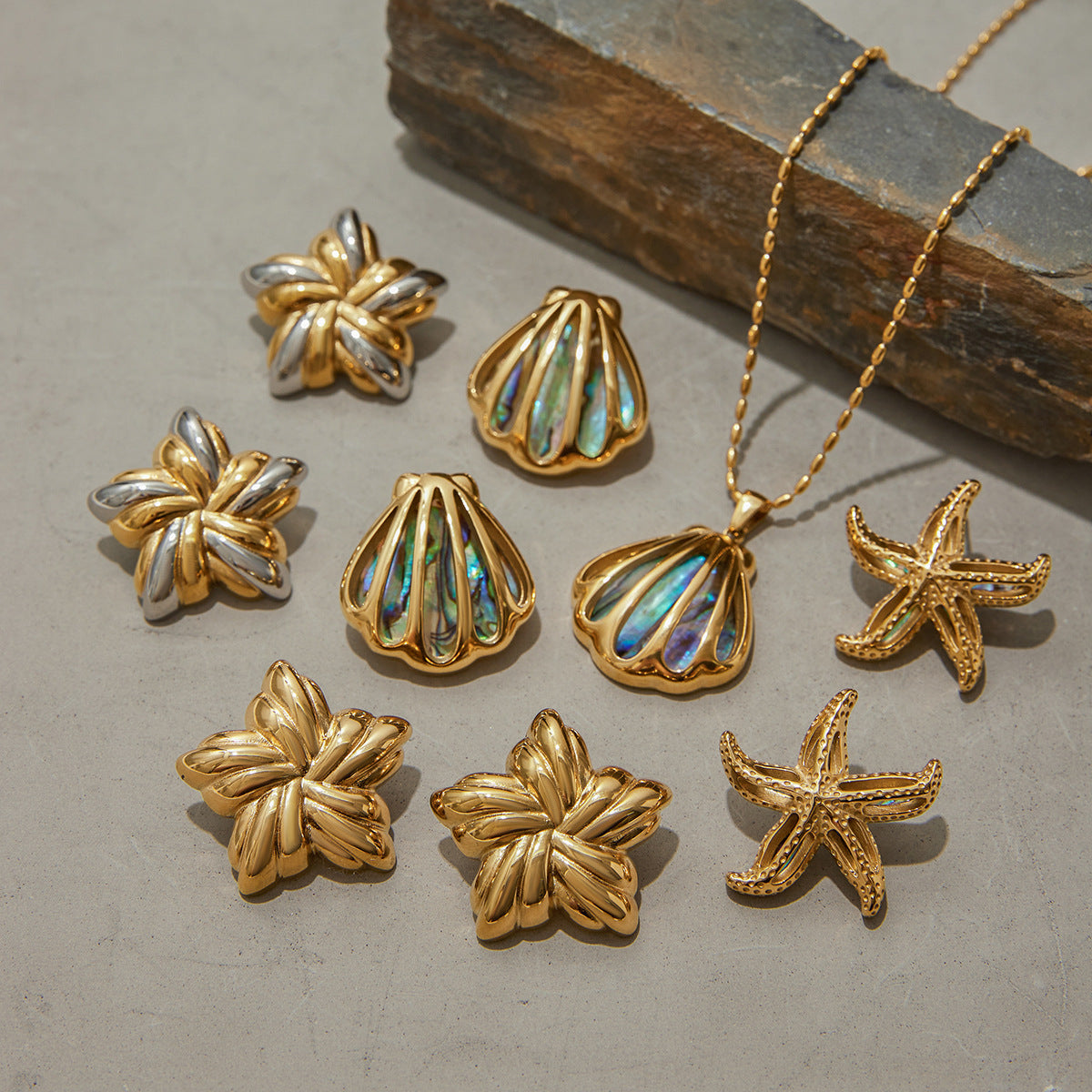 Flat lay of ocean-themed jewelry including shell and starfish pendants on stone background