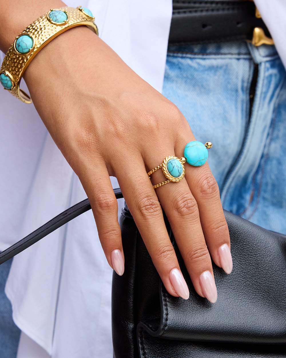 Hand wearing gold bracelets and rings with turquoise stones on a blurred background