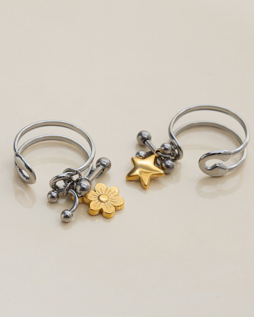 Three silver open rings with charms on a beige background