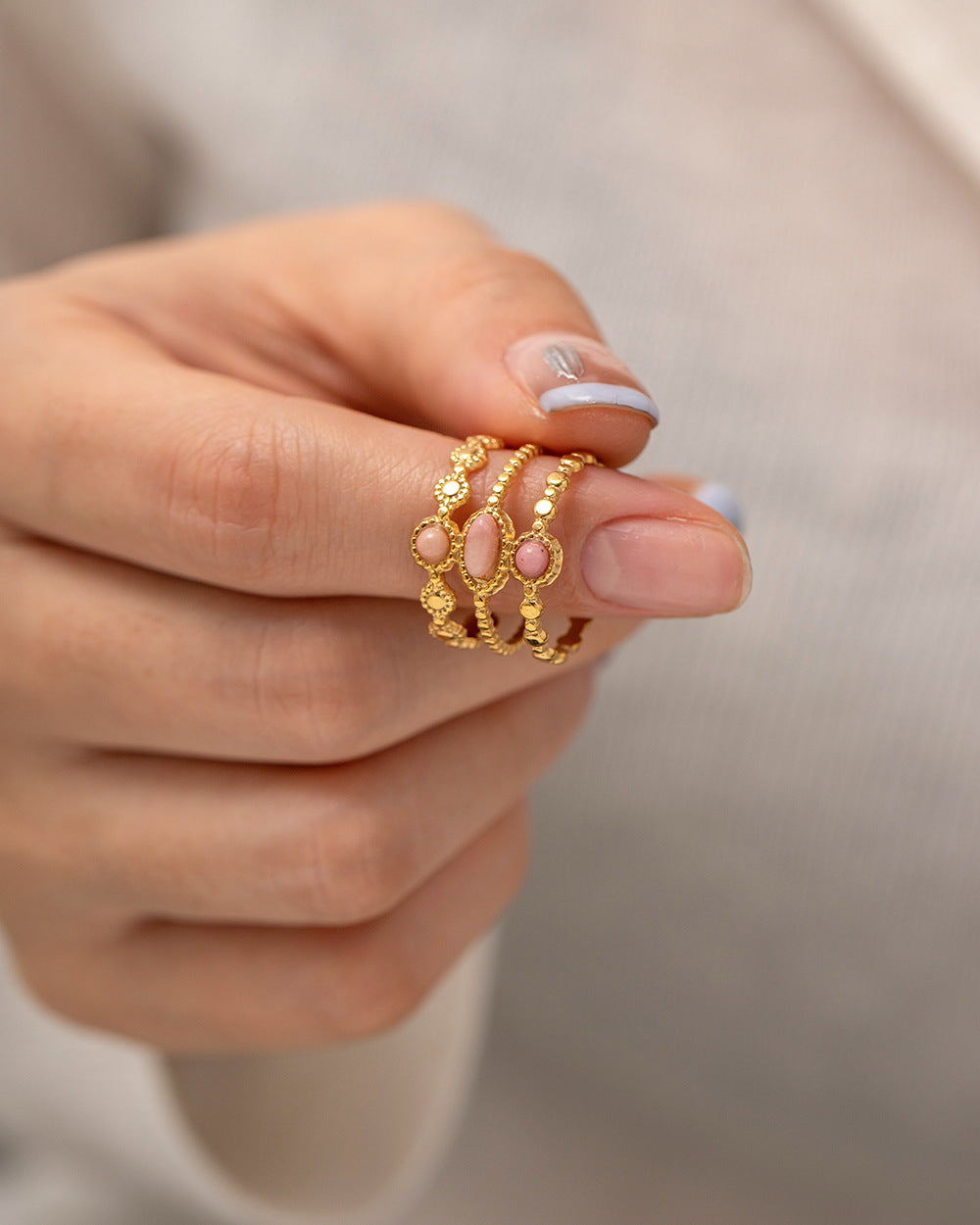 Gold ring with pink stones on a hand against a neutral background