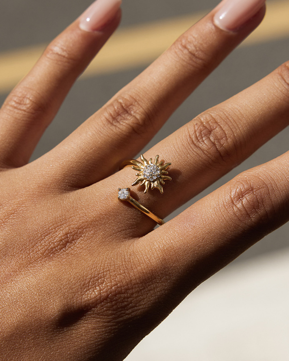 Hand wearing two rings with a sunflower design and diamond accents on a neutral background