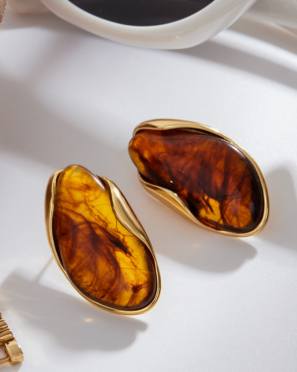 Gold-framed amber-colored stones on a white surface with a cup of coffee in the background.