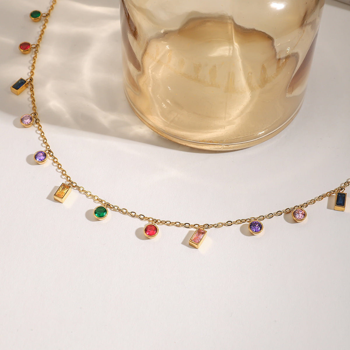 Detailed angled shot of colorful crystal necklace on gold chain, showing rectangular and round gemstone settings