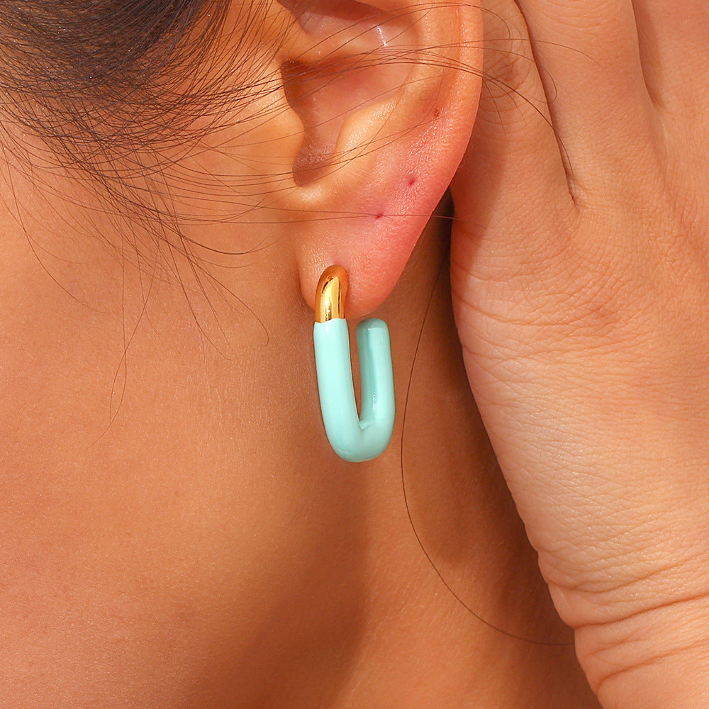 Single mint green and gold U hoop earring styled with hand pose on model’s face