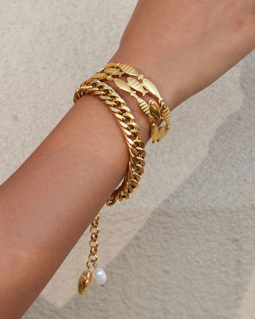 Gold bracelet with leaf design on a wrist against a neutral background