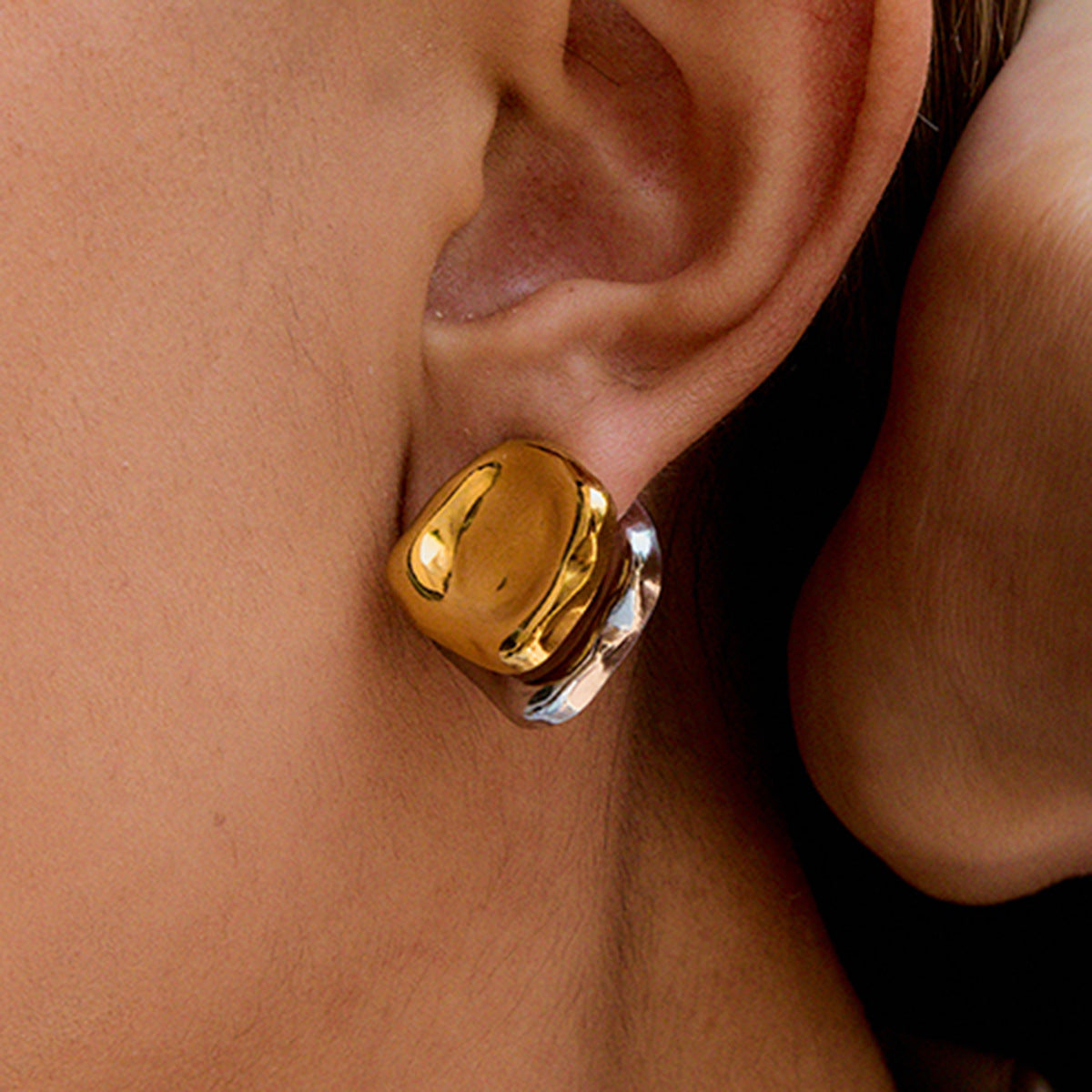 high-shine mixed metal earrings styled on ear, summer outdoor lighting