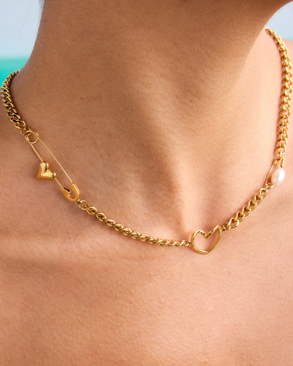 Detailed view of gold necklace with safety pin and open heart worn on neckline