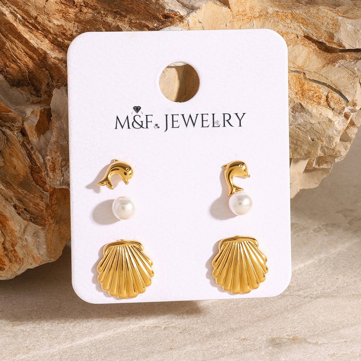 Three-pair gold-tone earring set including shell, pearl, and dolphin studs on branded M&F Jewelry card