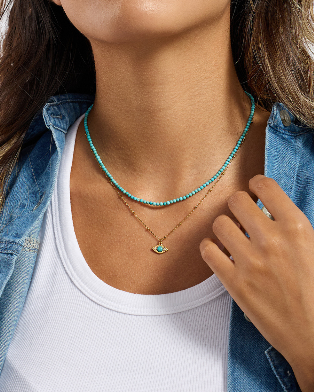 Person wearing a turquoise beaded necklace and a gold pendant necklace.