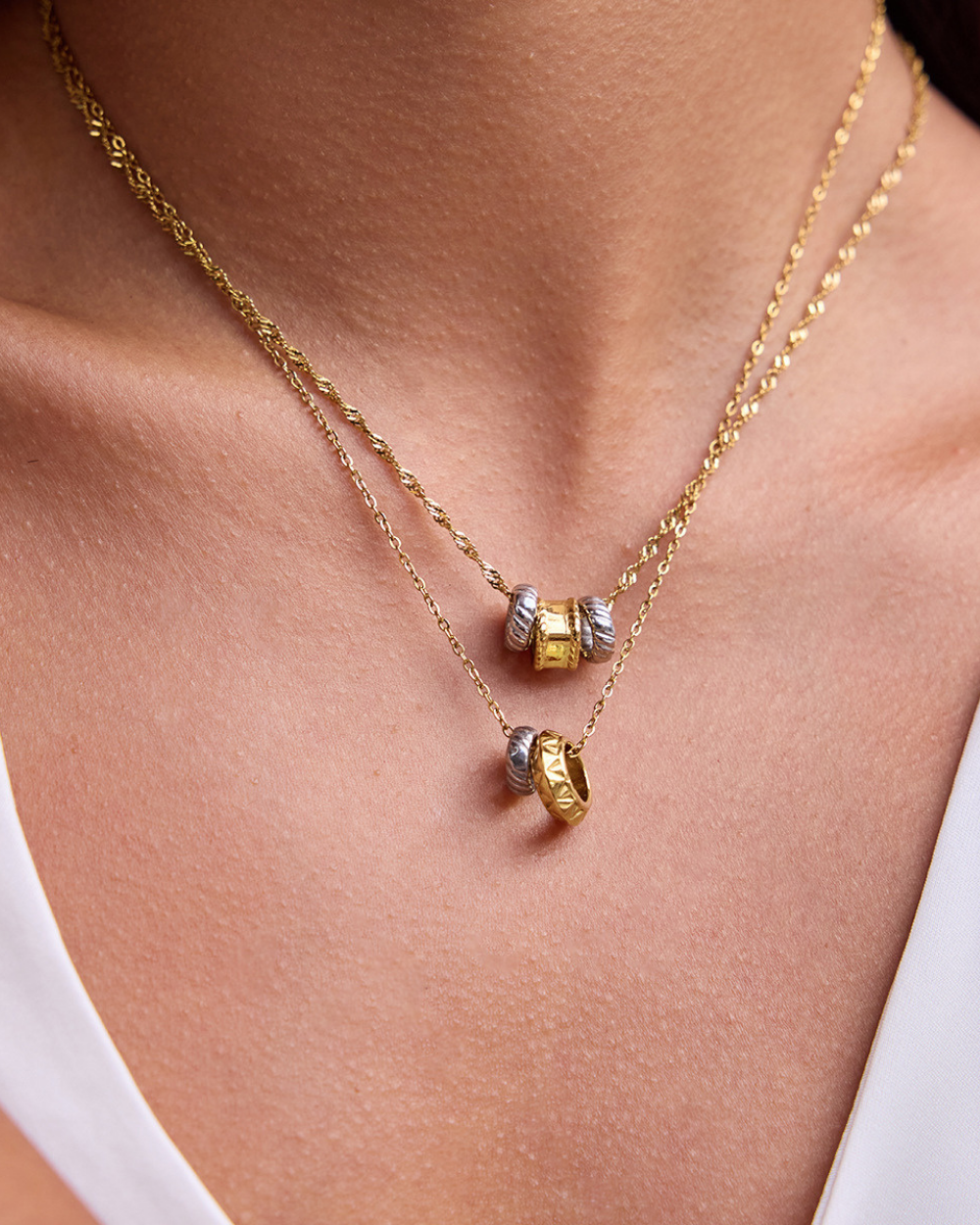 Gold necklace with beads on a person wearing a white top