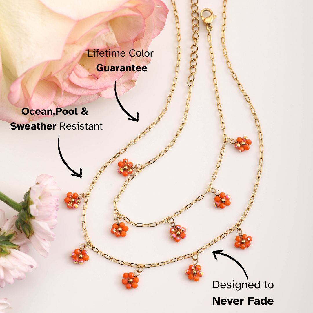 Gold daisy charm necklace with orange beads styled flatlay with roses – waterproof and color-safe summer jewelry