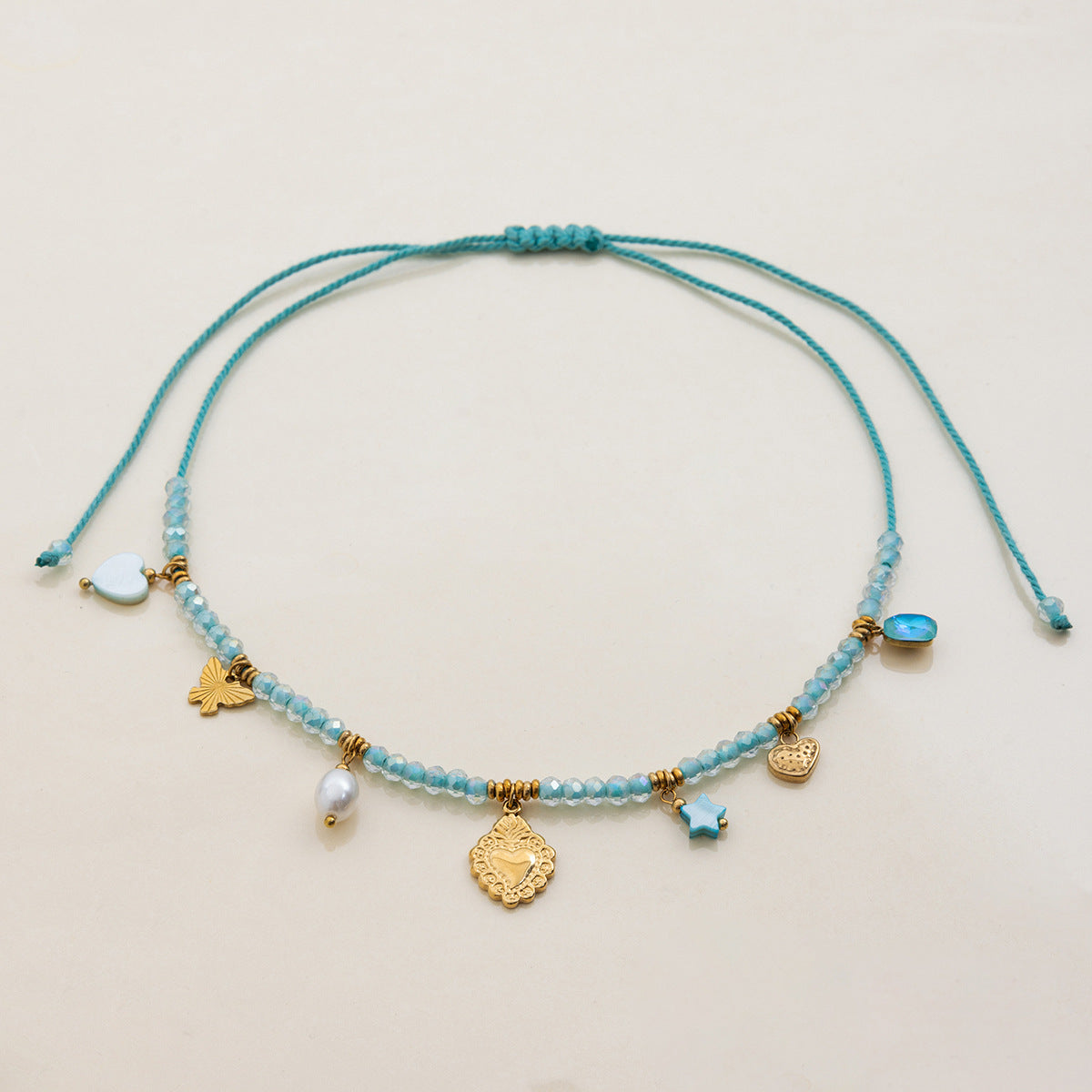 zoom on heart, butterfly and pearl charms on light blue crystal bead necklace