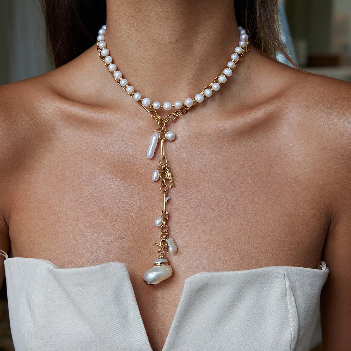 Pearl necklace with gold accents worn by a person in a white top.