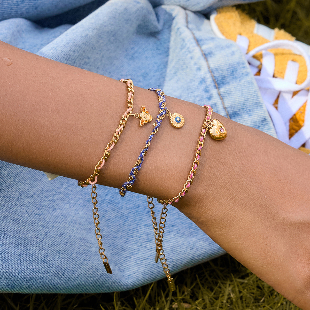 Close-up of a wrist wearing multiple gold bracelets with various charms against a denim background.