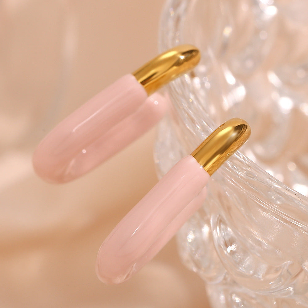 Light pink enamel and gold U earrings displayed elegantly on glass cup edge