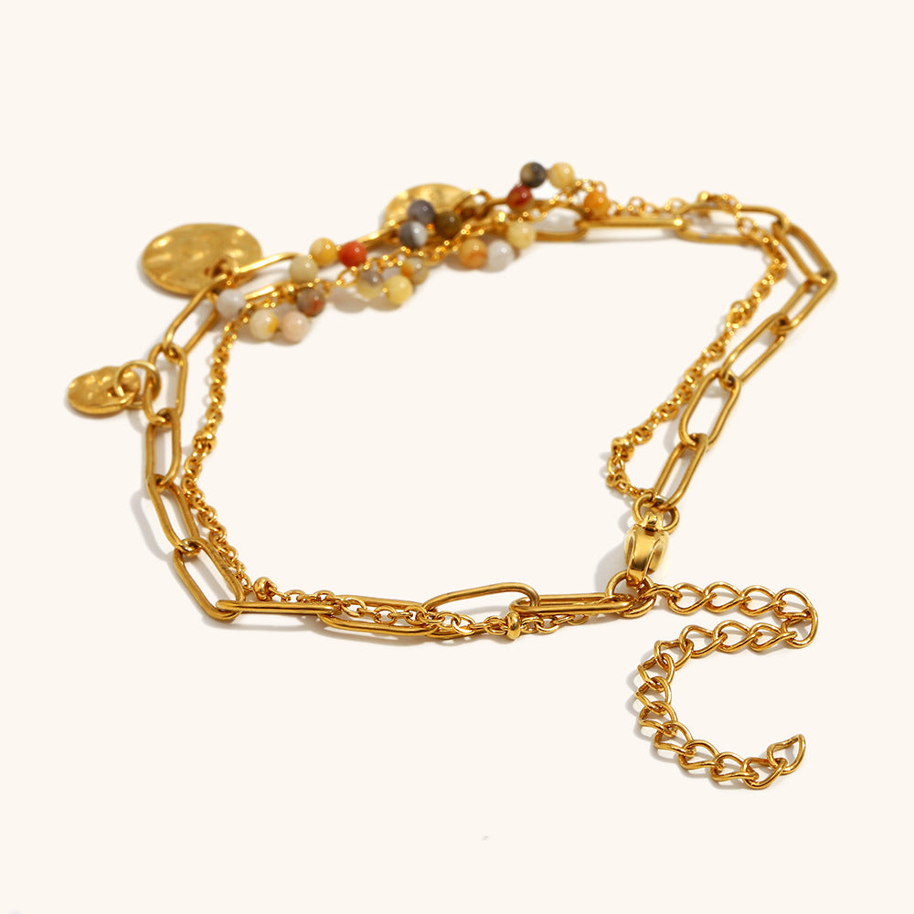 bohemian style bracelet with layered chain, coins, and beads on flat lay