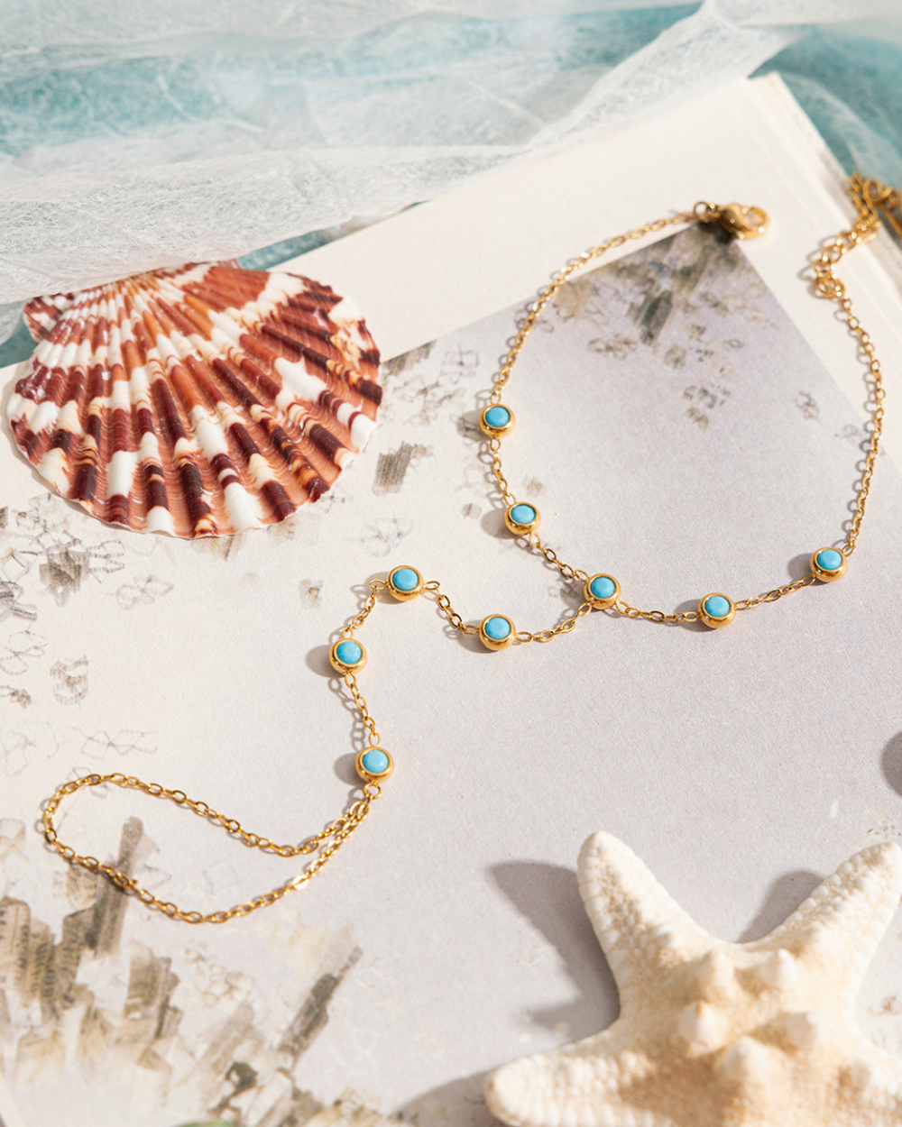 Gold necklace with turquoise stones on a shell and starfish background