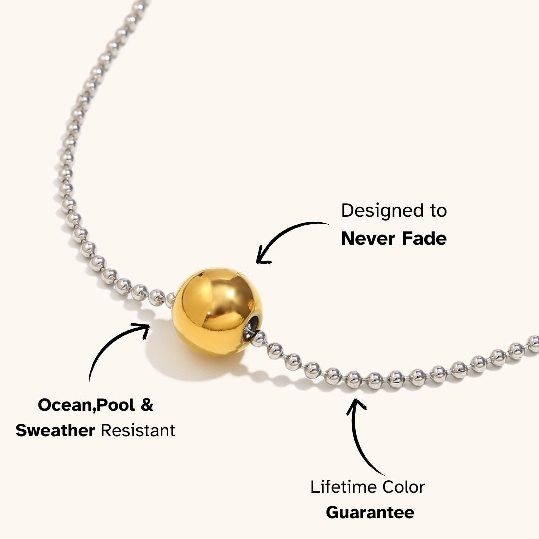 Close-up of silver bead necklace with gold orb pendant, labeled lifetime color safe