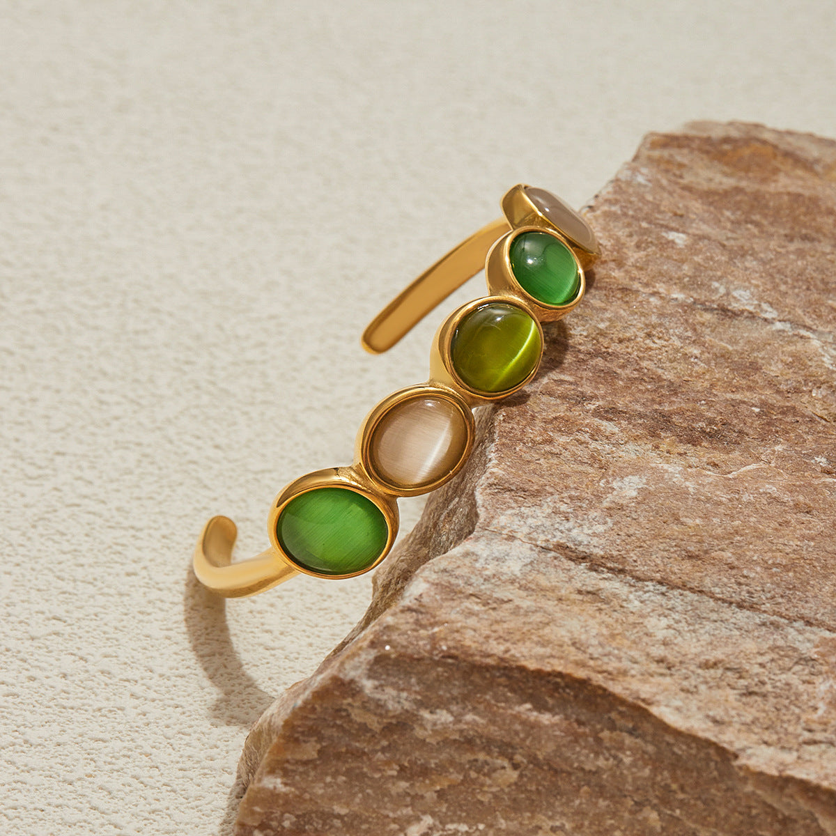 vintage gold bangle featuring mixed green and ivory cat-eye stones beside a rock