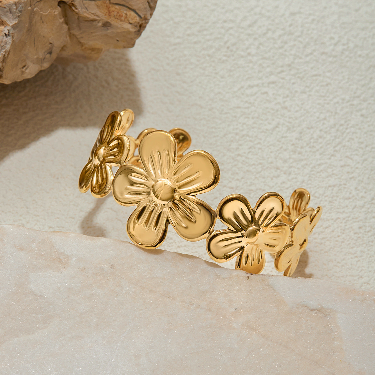 Close-up of a sculpted floral gold cuff bracelet on a light stone background