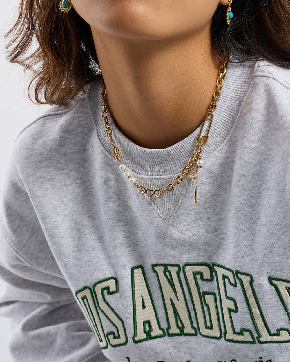 Gray sweatshirt with 'Los Angeles' text, gold necklace, and earrings on a neutral background