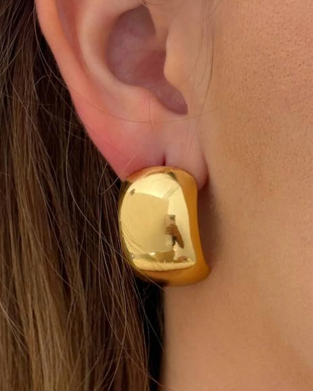Gold earring worn on an ear with a blurred background