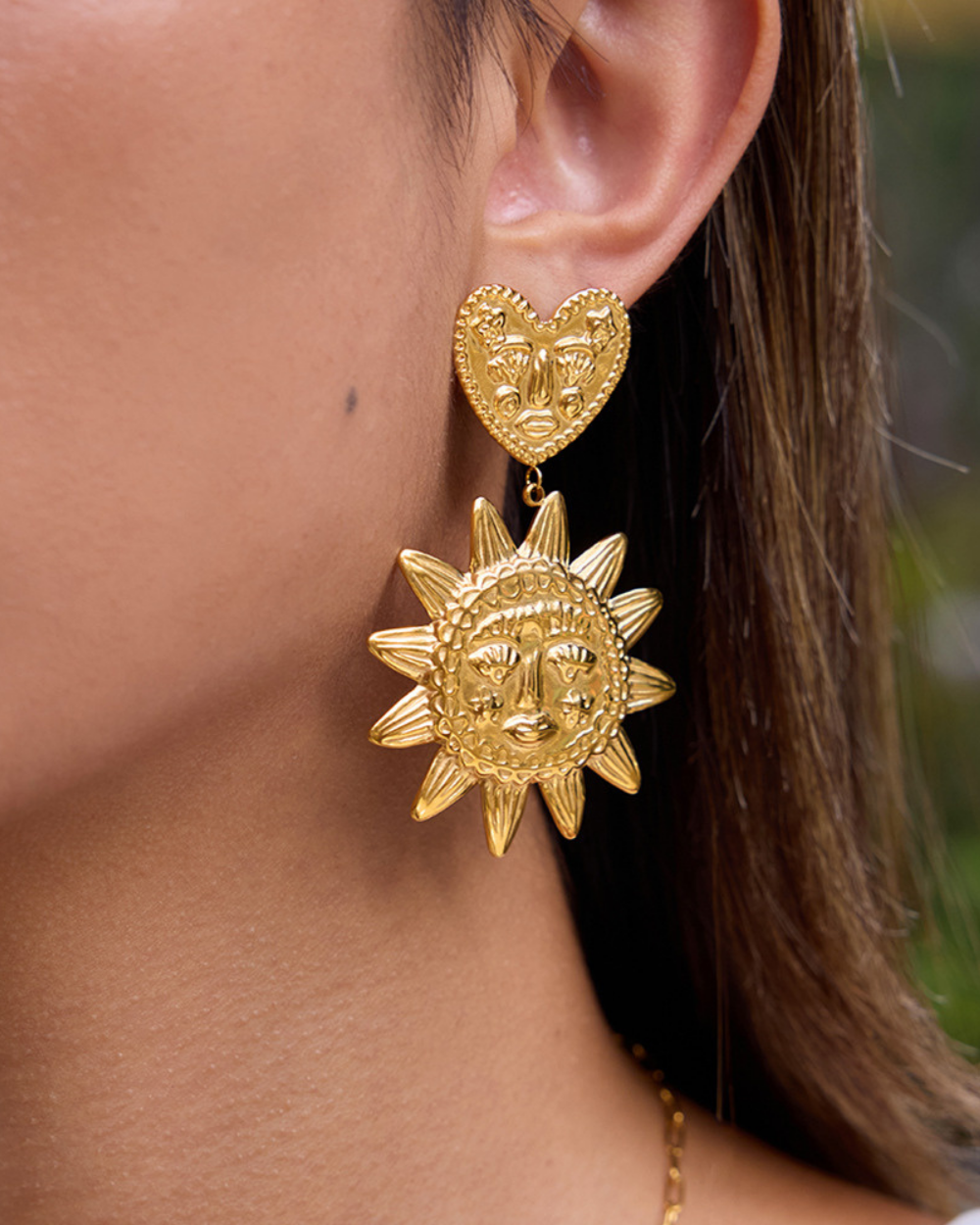 Gold heart-shaped earring with sun design worn by a person