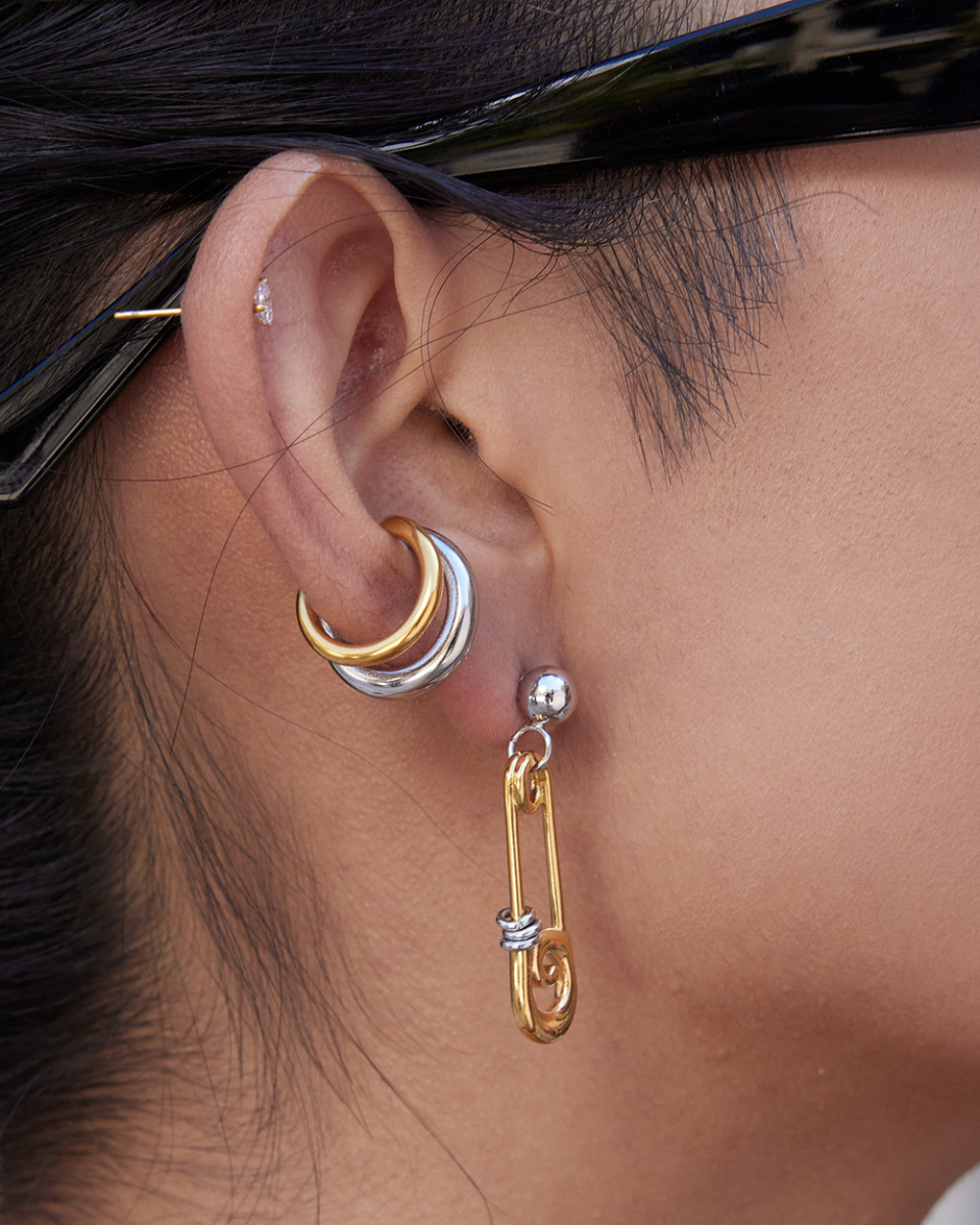 Close-up of an ear with gold and silver hoop earrings.