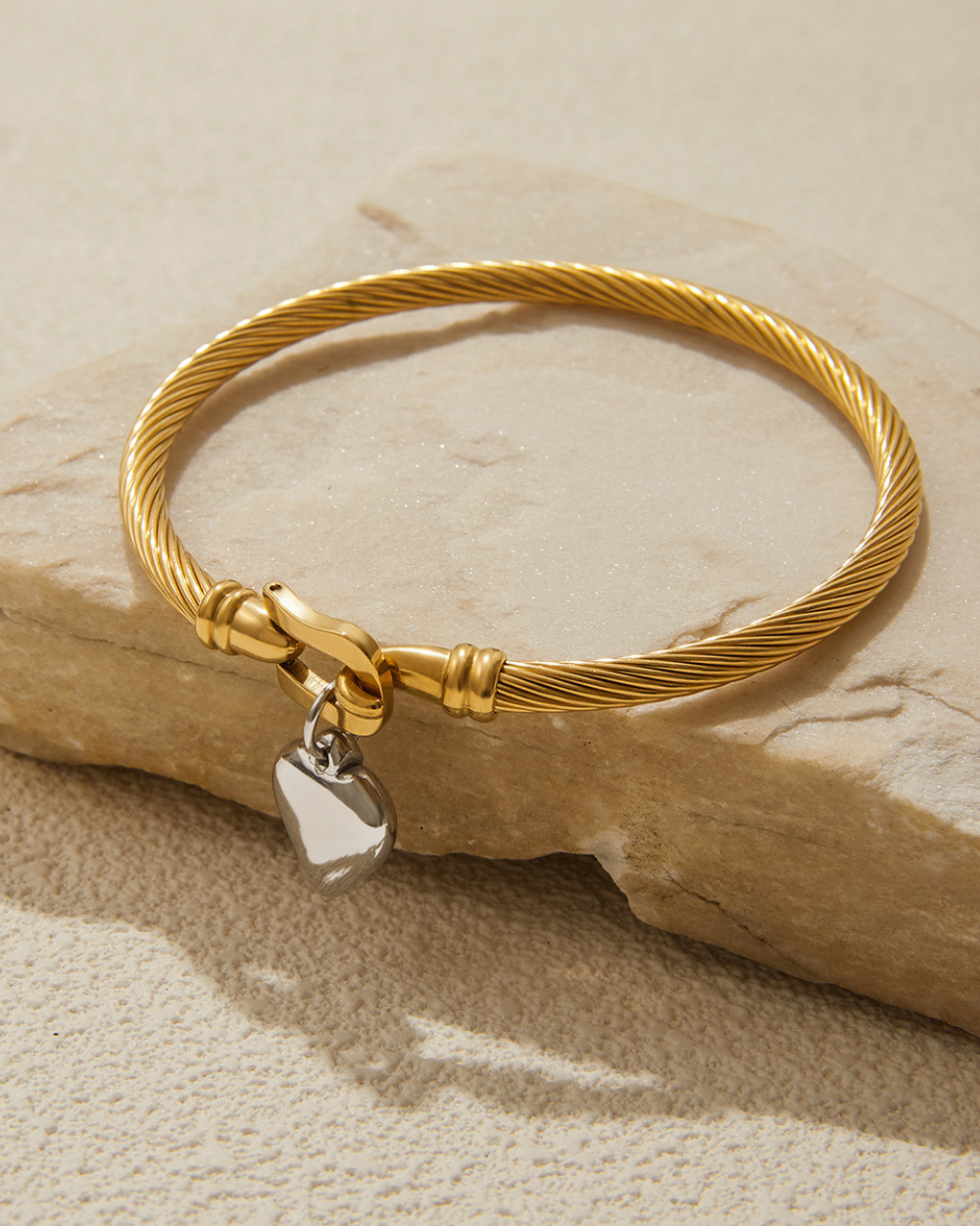Gold bracelet with a heart-shaped charm on a beige stone surface