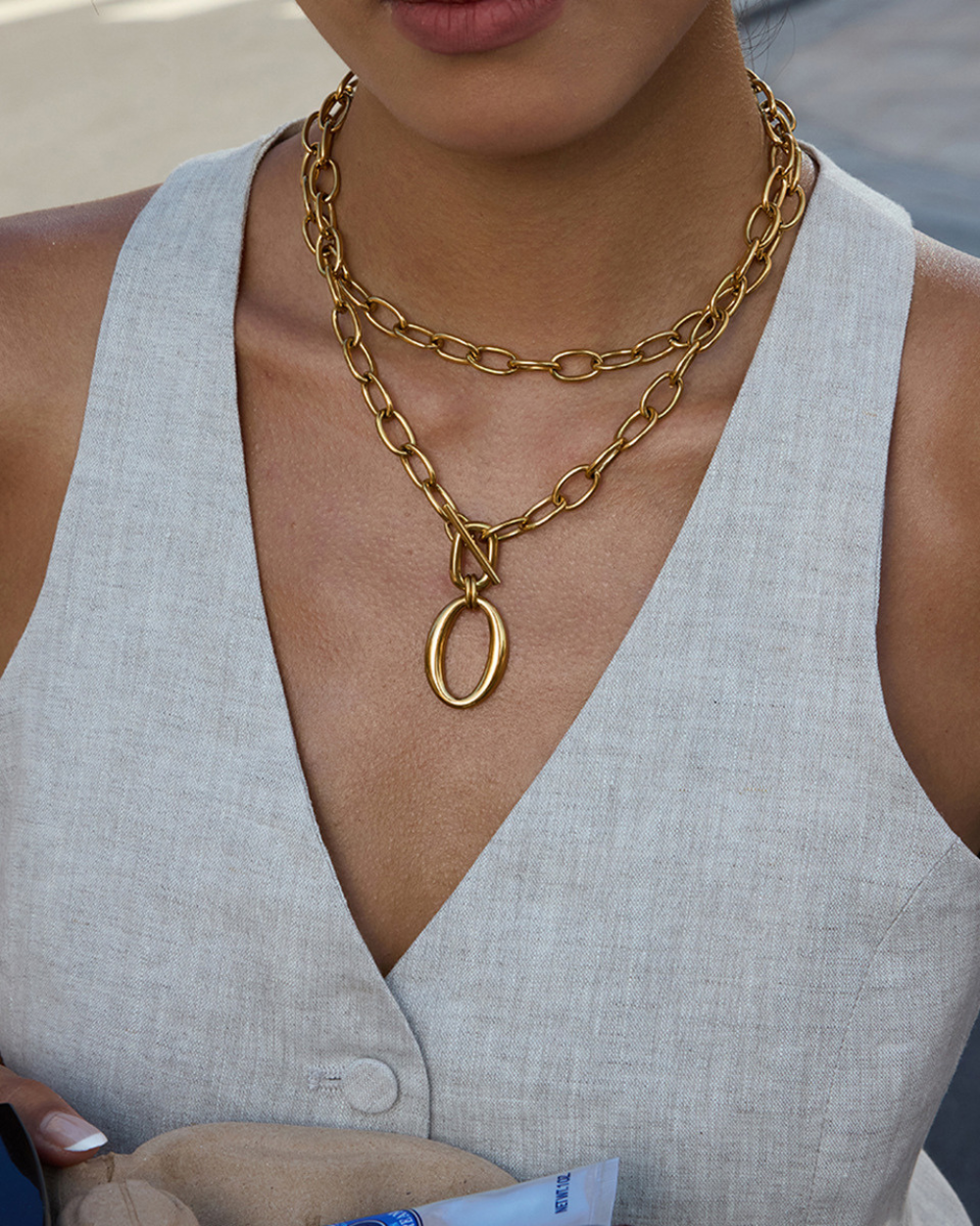 Person wearing a gold chain necklace with a pendant, dressed in a light gray sleeveless top.