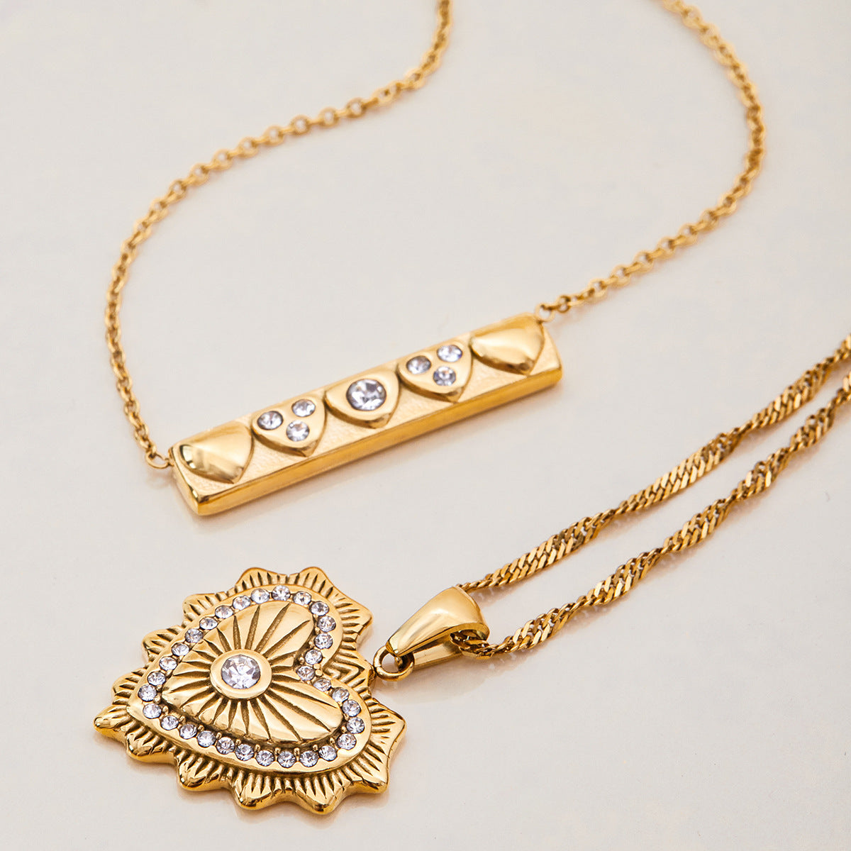 Layered necklaces with textured gold heart and crystal-embellished bar, shown together