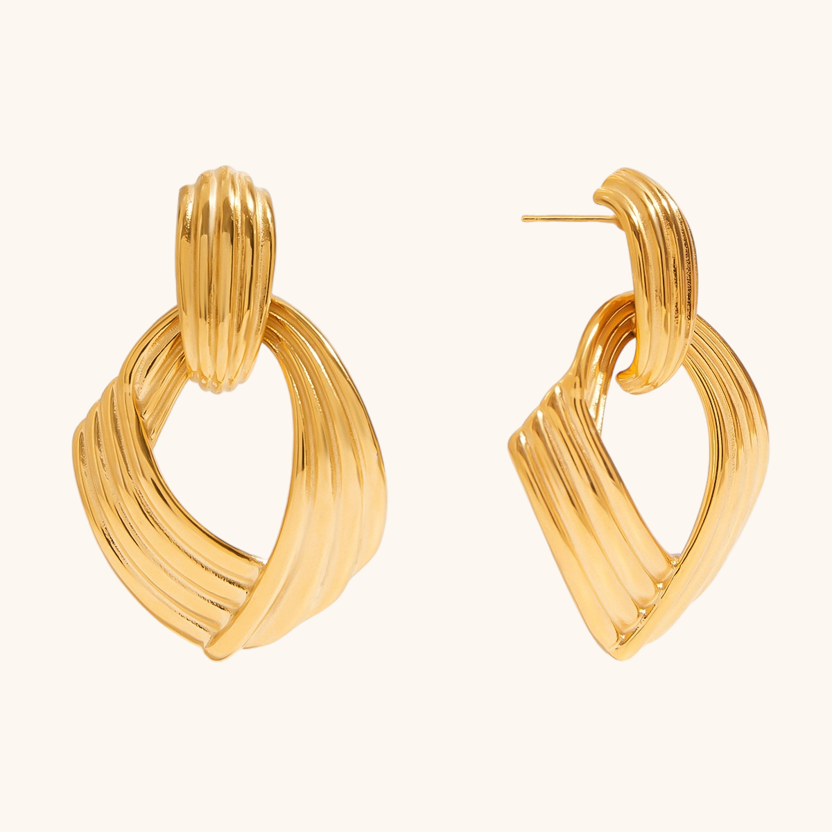 Bold gold twisted drop earrings with textured surface, laid flat on beige background