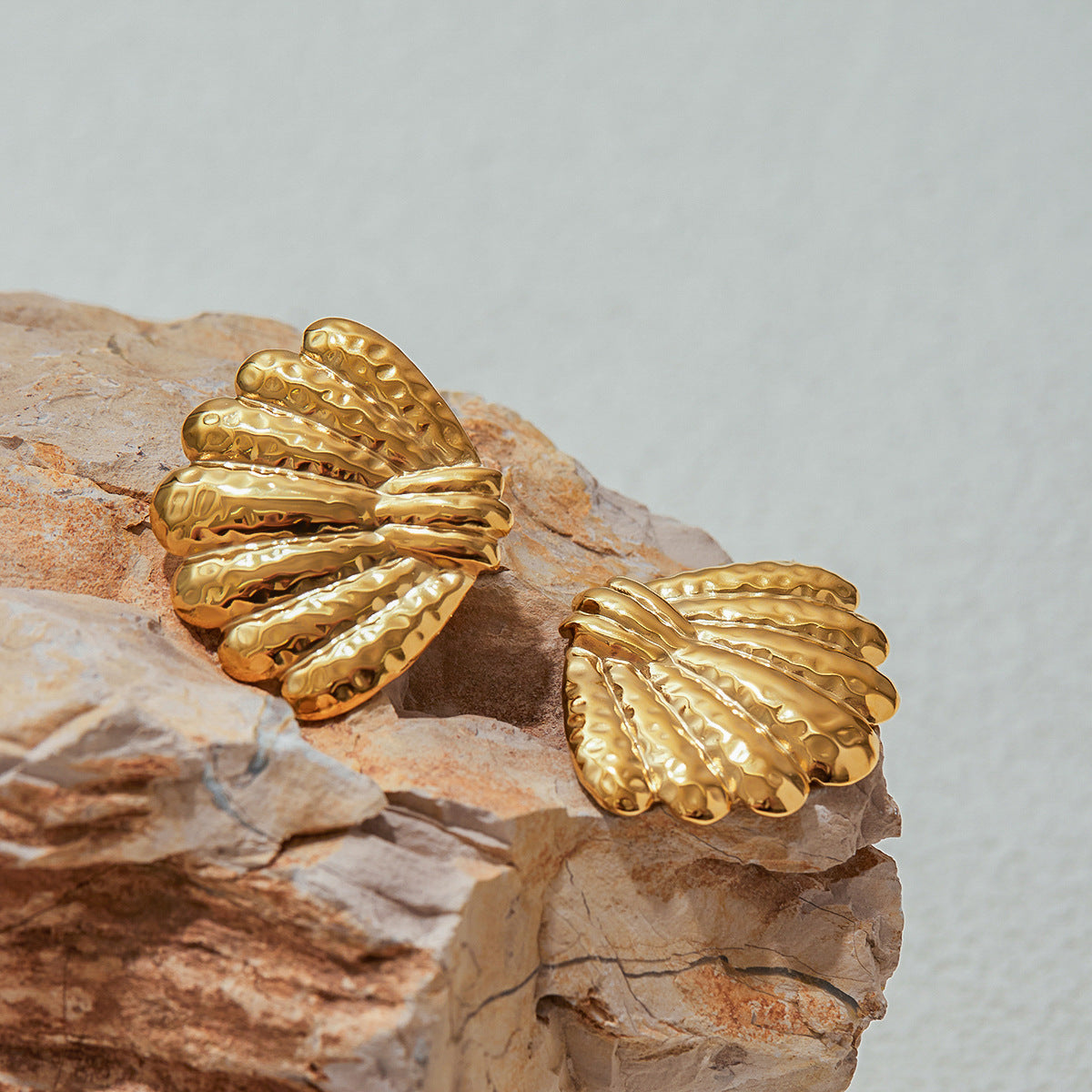 Close-up of textured gold shell earrings on natural rock background