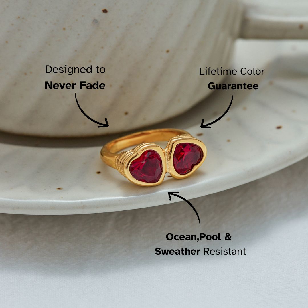 Gold open band ring with double red heart-shaped gemstones on a ceramic plate