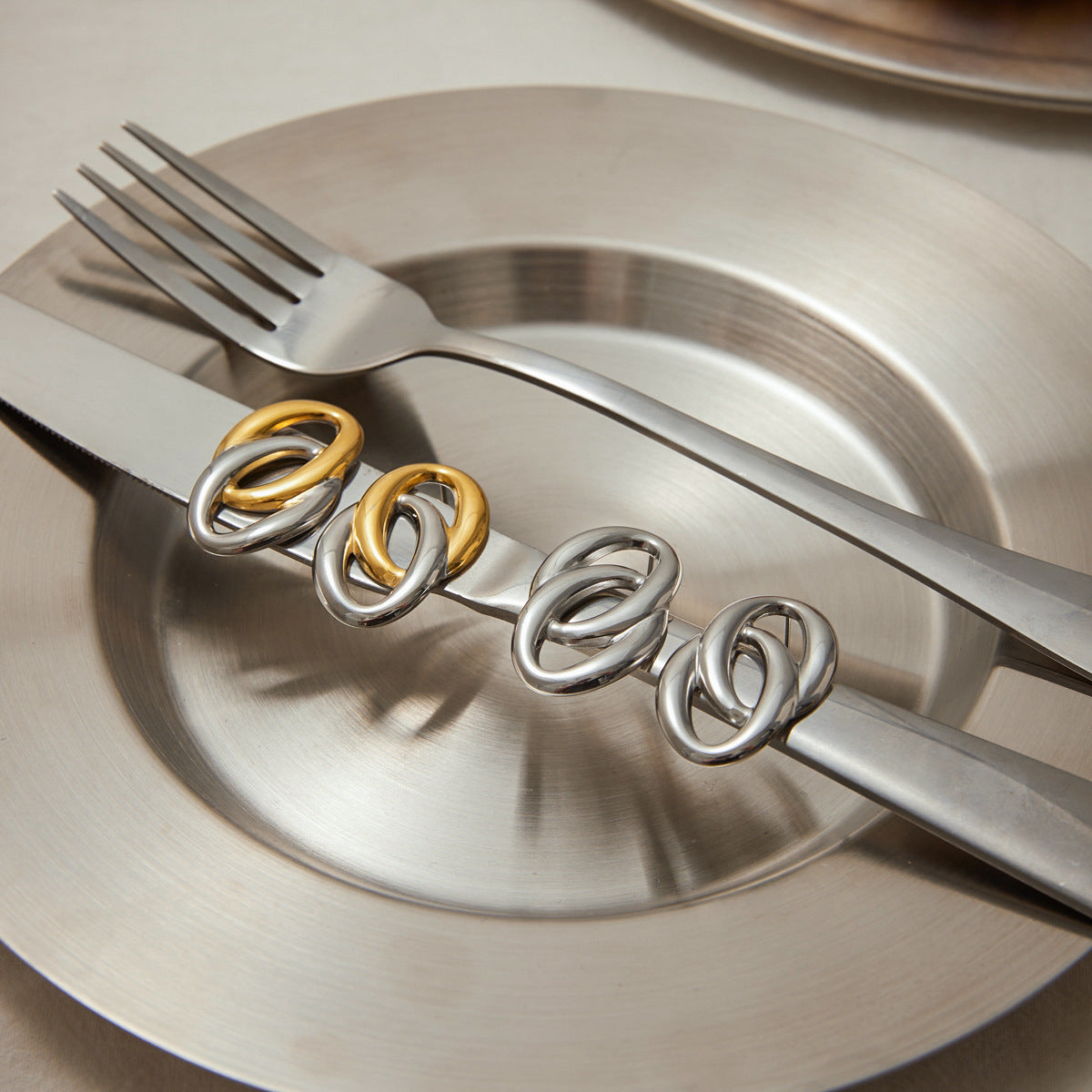 Silver and gold chunky hoop earrings arranged on a knife and fork over silver plate