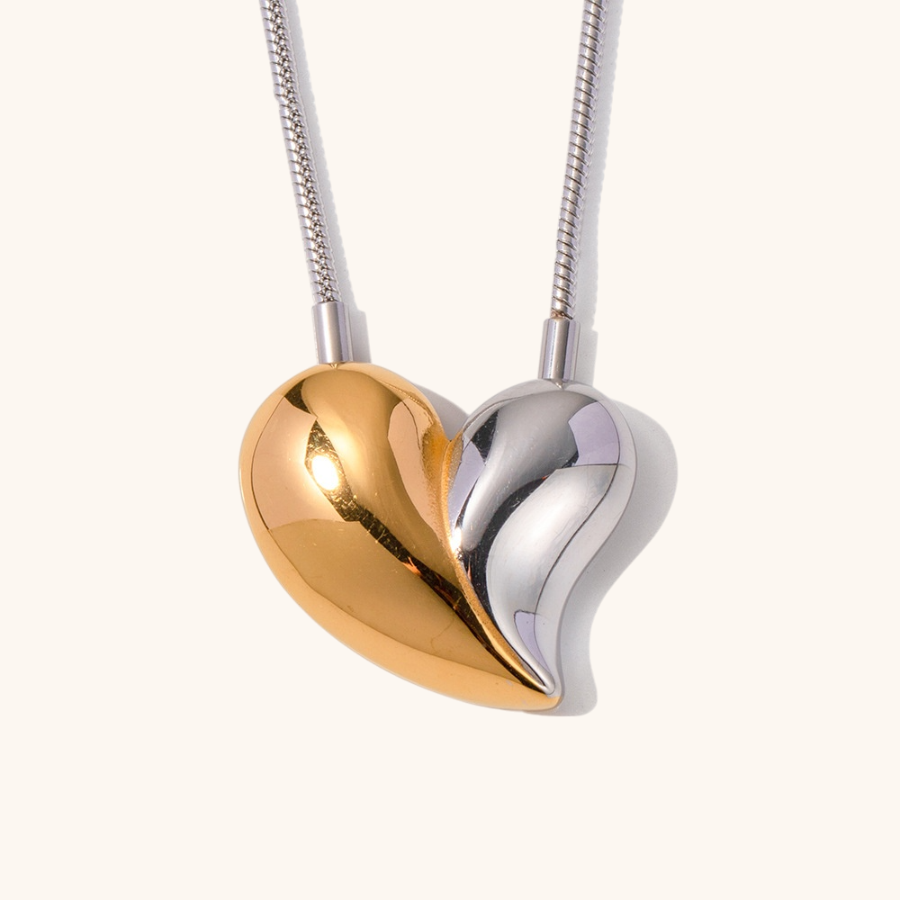 Close-up of gold sculptural heart necklace on soft lighting and cream backdrop