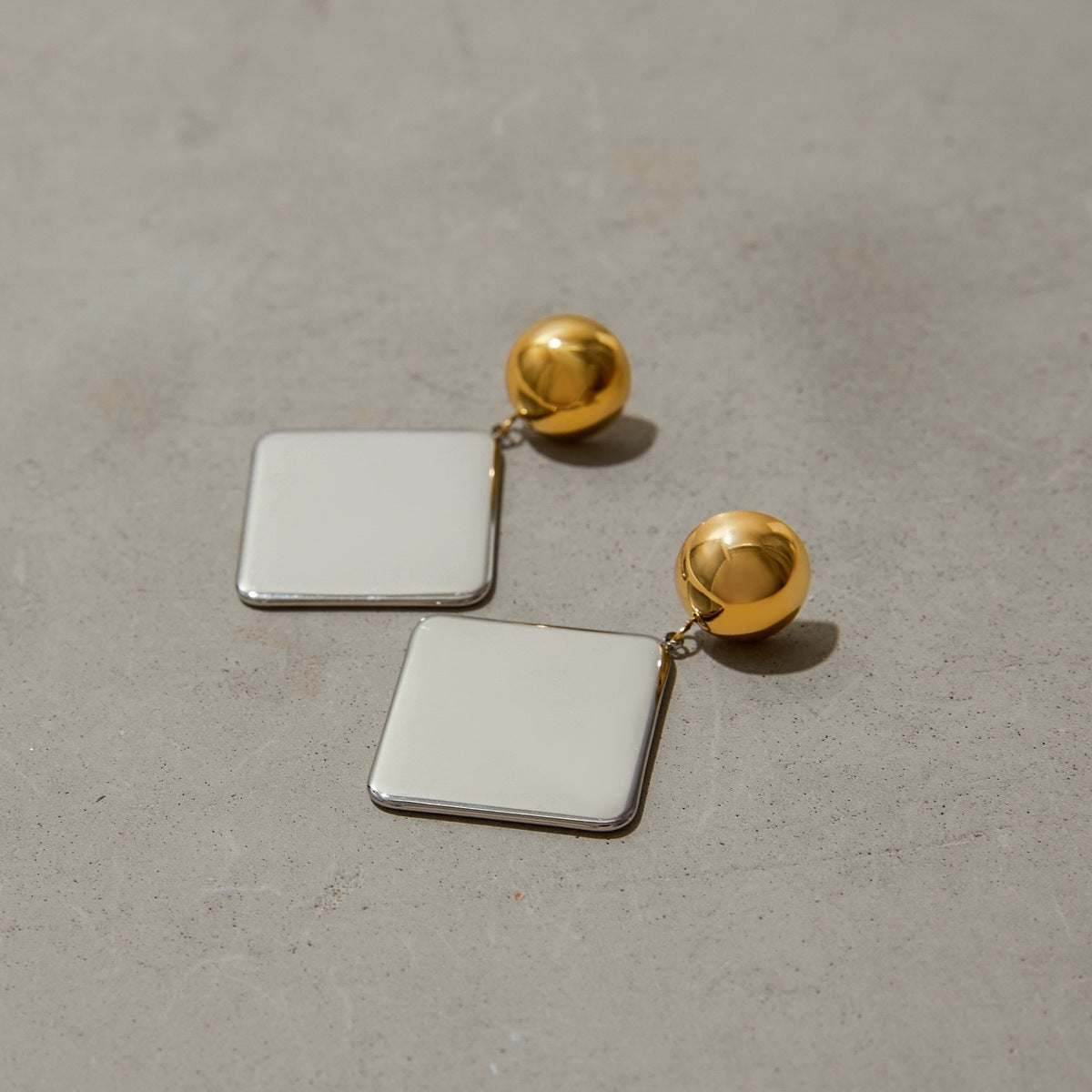 Modern square drop earrings in gold and silver, displayed on stone