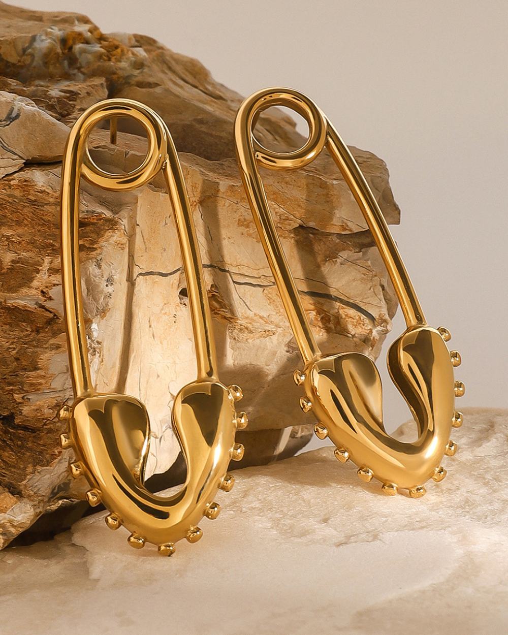 Gold safety pin earrings on a textured stone surface