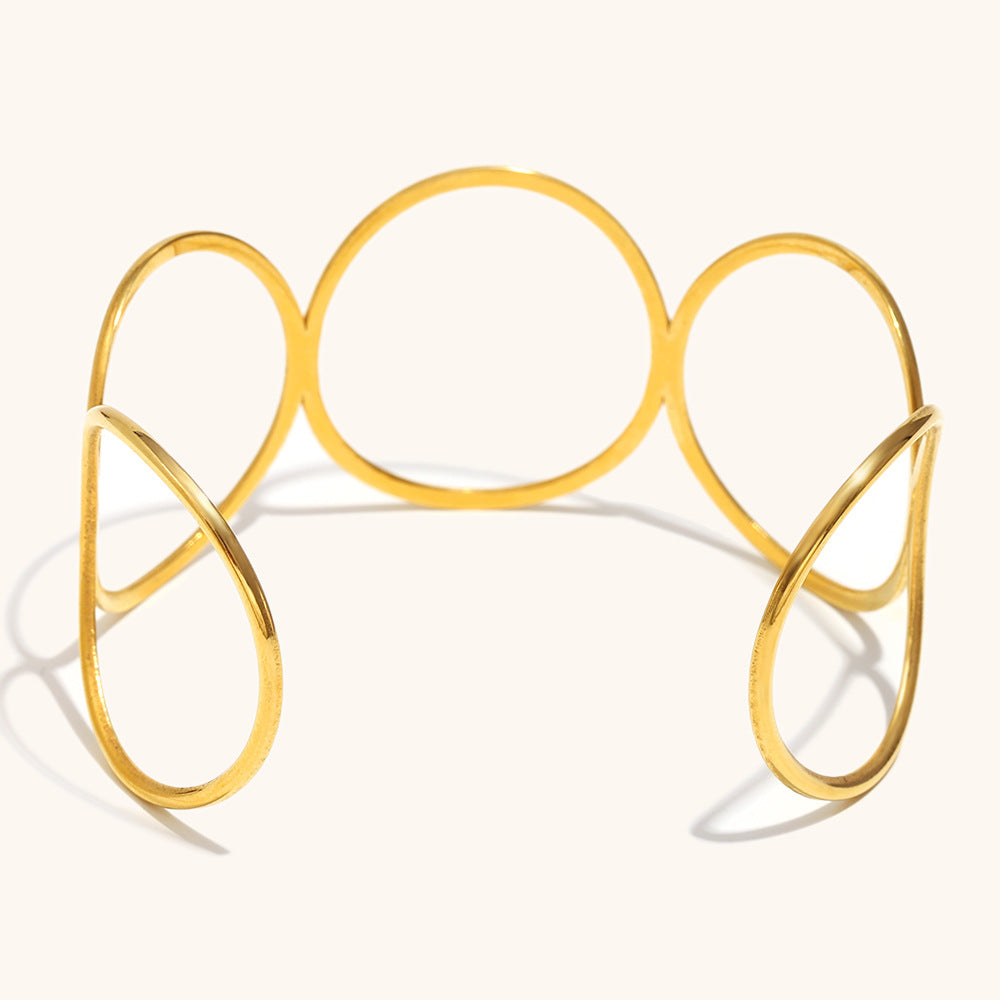 Sculptural gold metal cuff bracelet with open loops and negative space design, artistic layout shot.