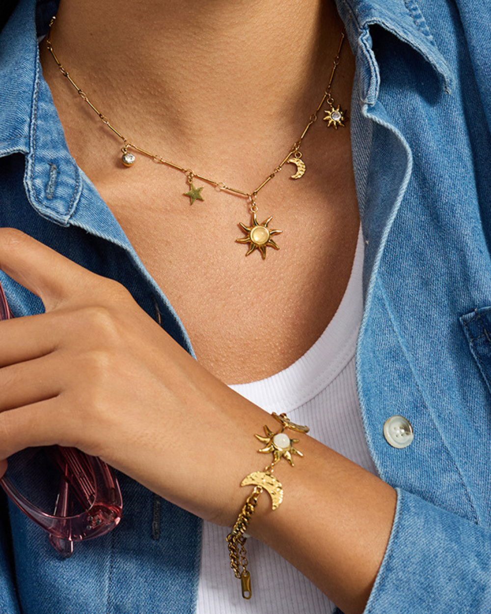 Gold necklace and bracelet with celestial charms worn by a person in a denim jacket.