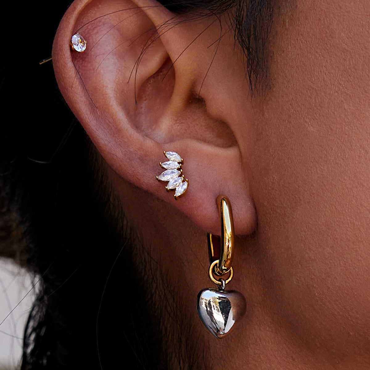Close-up of an ear wearing gold hoop earrings with heart pendants.