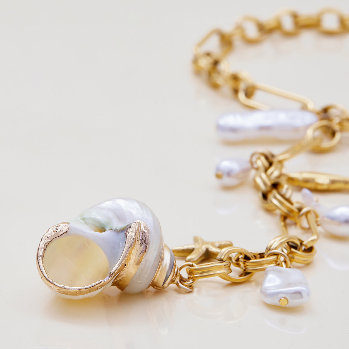 Gold chain bracelet with pearl charms on a light background