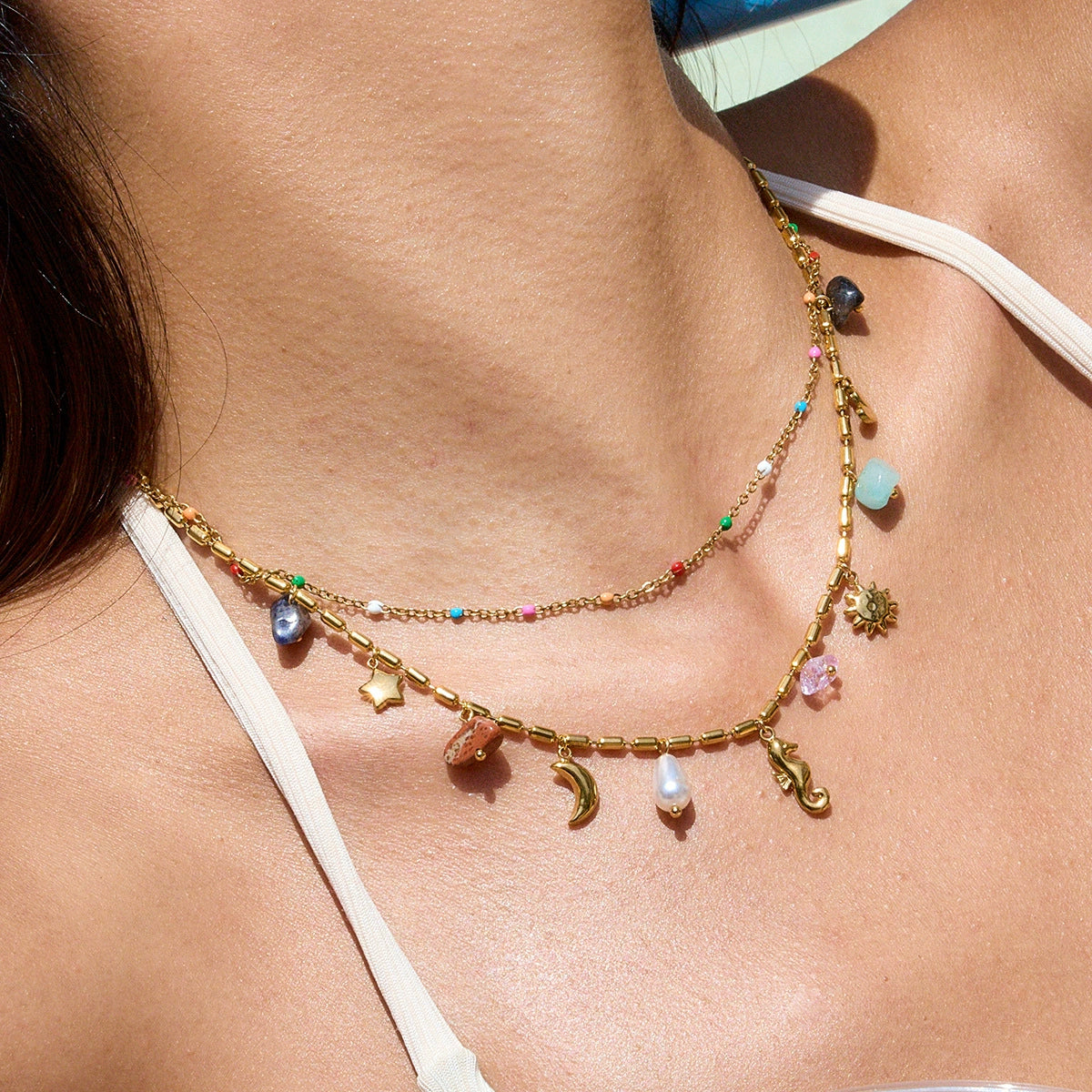 Necklace with colorful charms on a person wearing a white bikini top.